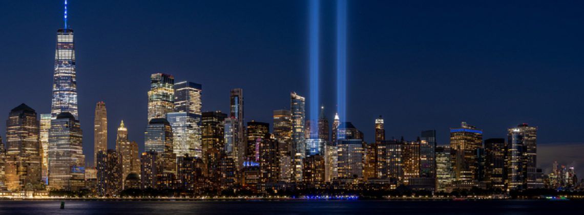 New York skyline with lights coming up from the 9/11 memorial at night.